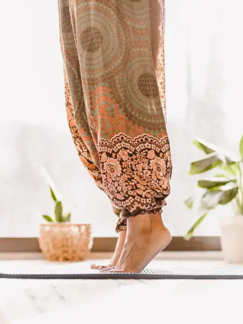 Image of a woman's legs wearing harem yoga pants as she raises up on her toes standing on a yoga mat.