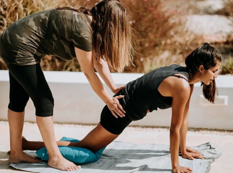 Yoga teacher helping a student by adjusting her alignment