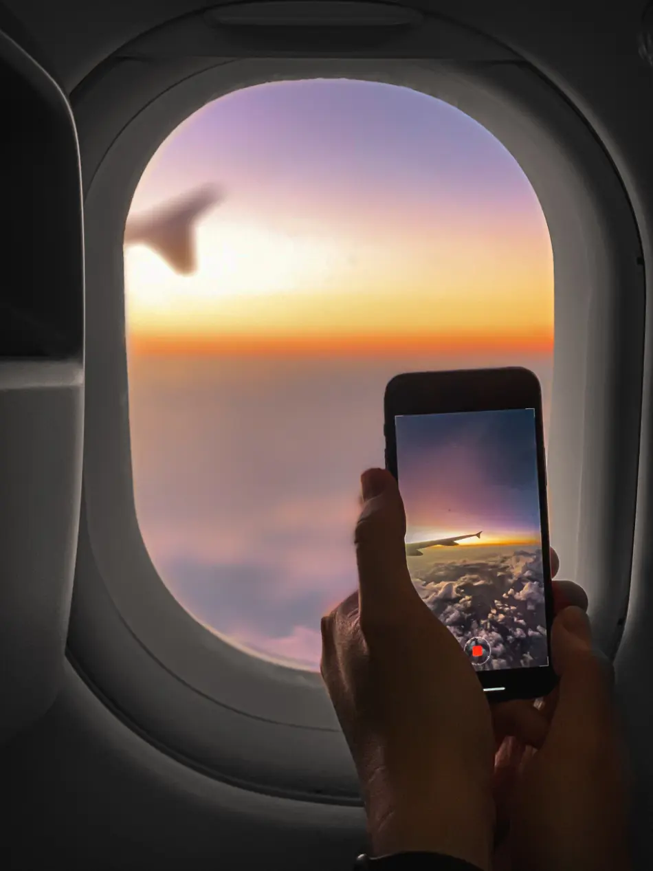 View of a person capturing a video out of the window of an airplane. The horizon appears to be sunset with purples and oranges on the sky.