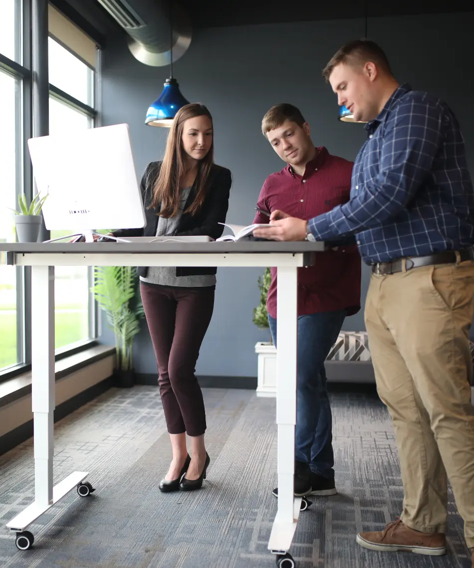 Woman and two coworkers at a standing desk discussing work related things.